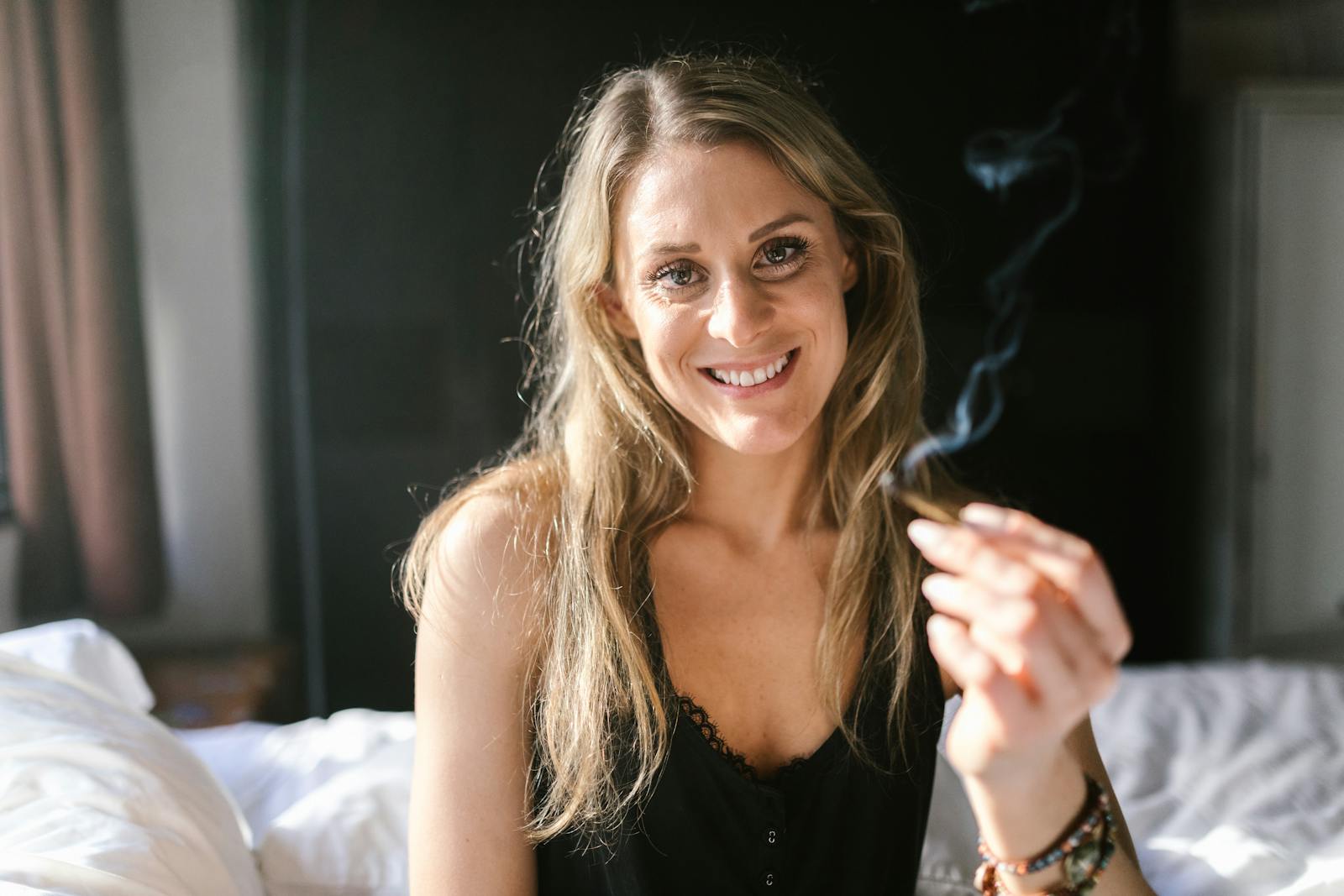 Smiling woman holding a joint, embracing cannabis culture in a relaxed indoor setting.