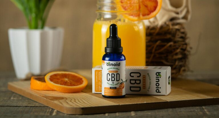 Colorful CBD oil and fresh orange juice on a wooden table, showcasing product photography.