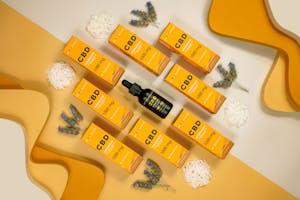 Flat lay of CBD boxes and vials with lavender on a yellow background, perfect for wellness themes.