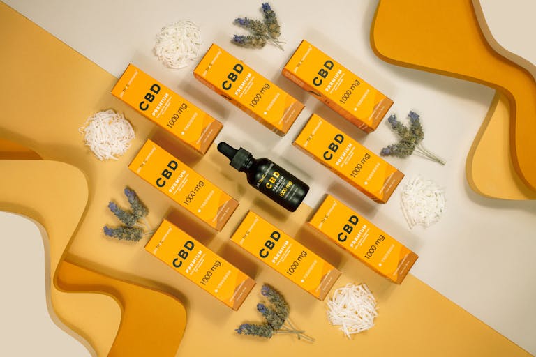 Flat lay of CBD boxes and vials with lavender on a yellow background, perfect for wellness themes.