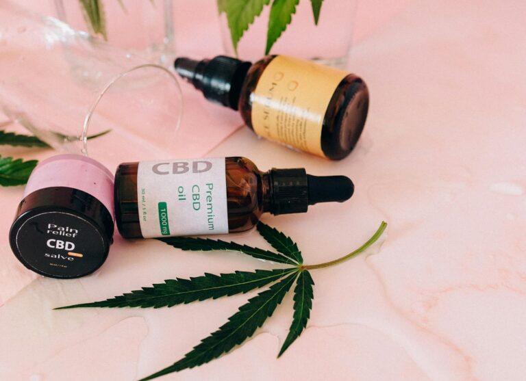 Stylish flat lay featuring CBD oil bottles and hemp leaves on a pink background.
