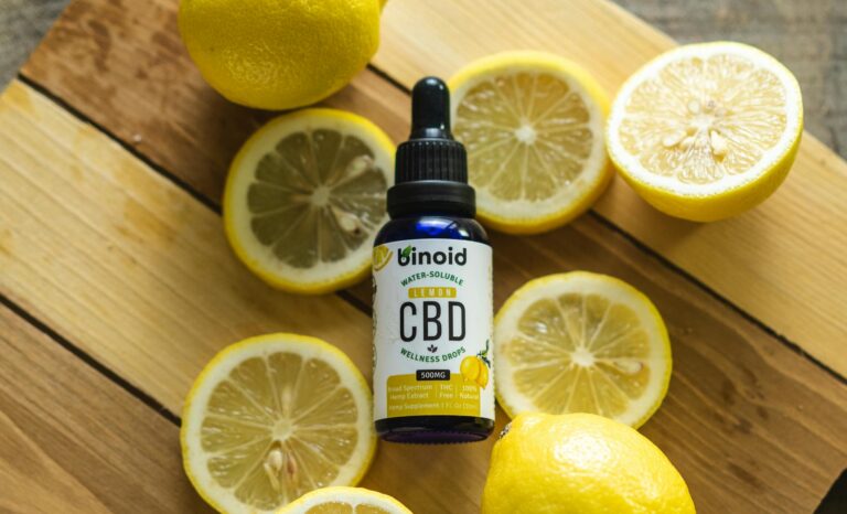 Top view of sliced fresh lemons surrounding a bottle of CBD oil on a rustic wooden board.